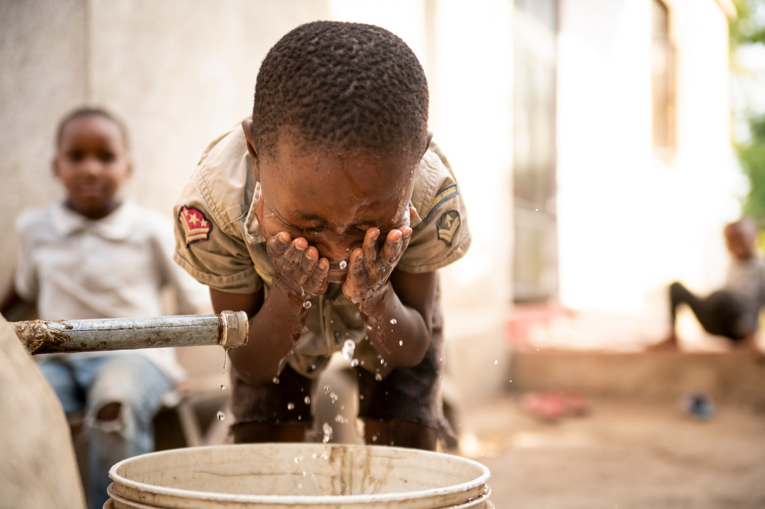 A boy splashes water on his face from his family's rainwater harvesting system.